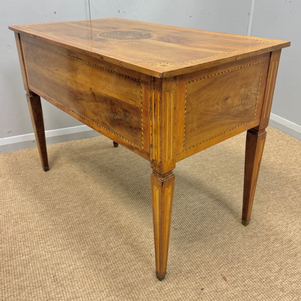 An early nineteenth-century freestanding wood writing desk featuring intricate marquetry inlays, five drawers with brass handles, an arched kneehole, and square tapered legs. View IX