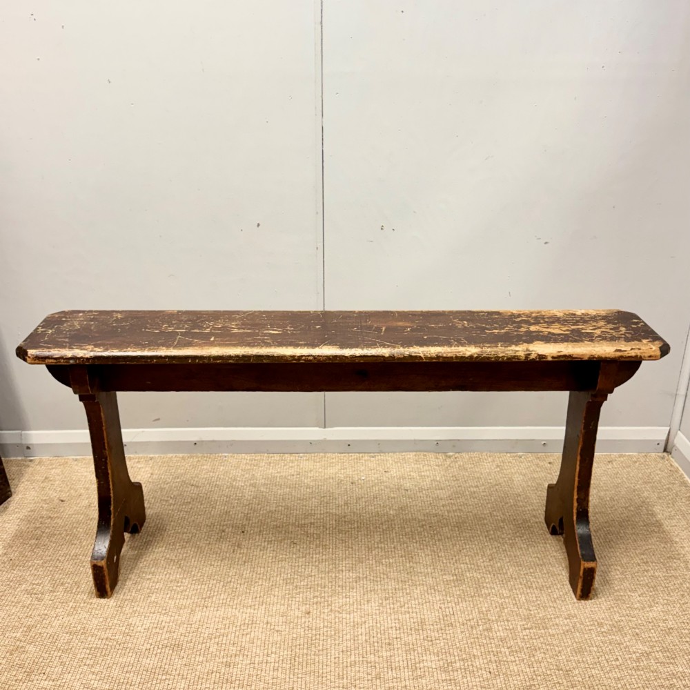 A five-foot antique pine bench featuring a distressed dark brown finish and shaped slab end supports.