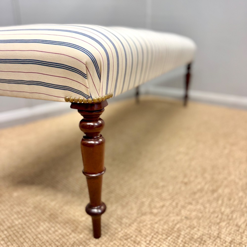 A five-foot long upholstered bench featuring cream and blue ticking stripe fabric, deep buttoning, brass stud trim, and dark turned timber legs. View II