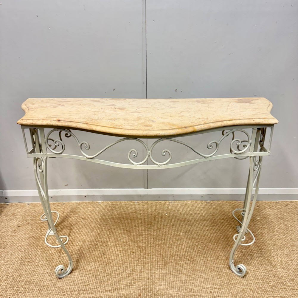 A French wrought iron console table featuring a contoured beige marble top set upon an off-white painted frame with decorative scrollwork.