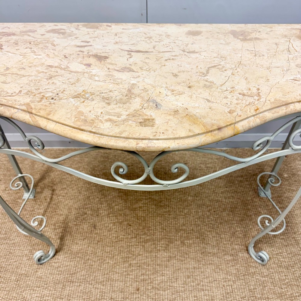 A French wrought iron console table featuring a contoured beige marble top set upon an off-white painted frame with decorative scrollwork. View II