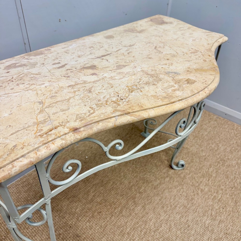 A French wrought iron console table featuring a contoured beige marble top set upon an off-white painted frame with decorative scrollwork. View III