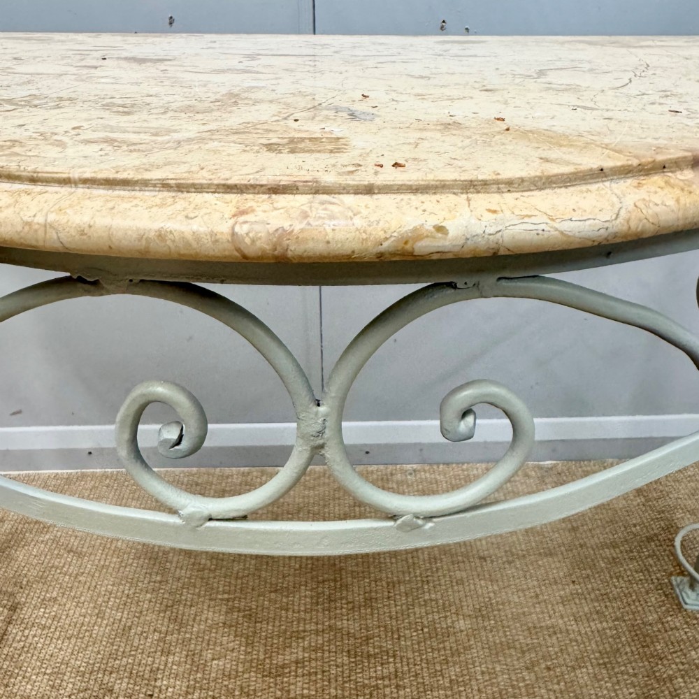 A French wrought iron console table featuring a contoured beige marble top set upon an off-white painted frame with decorative scrollwork. View VII