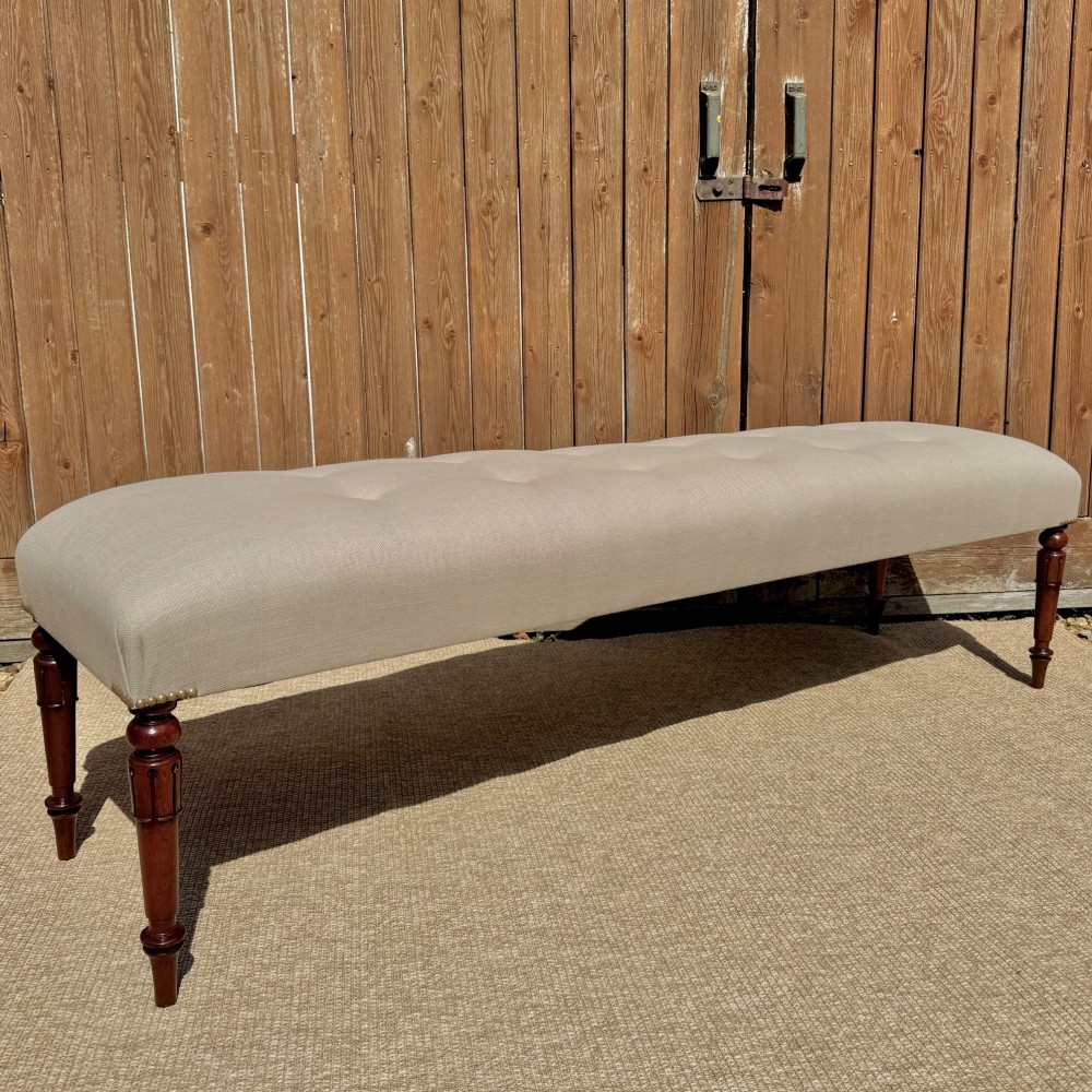 A long 185cm upholstered stool featuring a beige button-tufted linen top set on four turned dark wood legs. View II