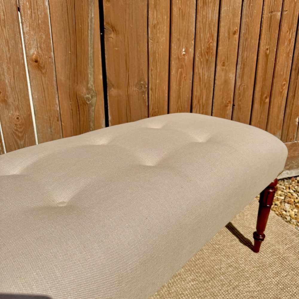 A long 185cm upholstered stool featuring a beige button-tufted linen top set on four turned dark wood legs. View III