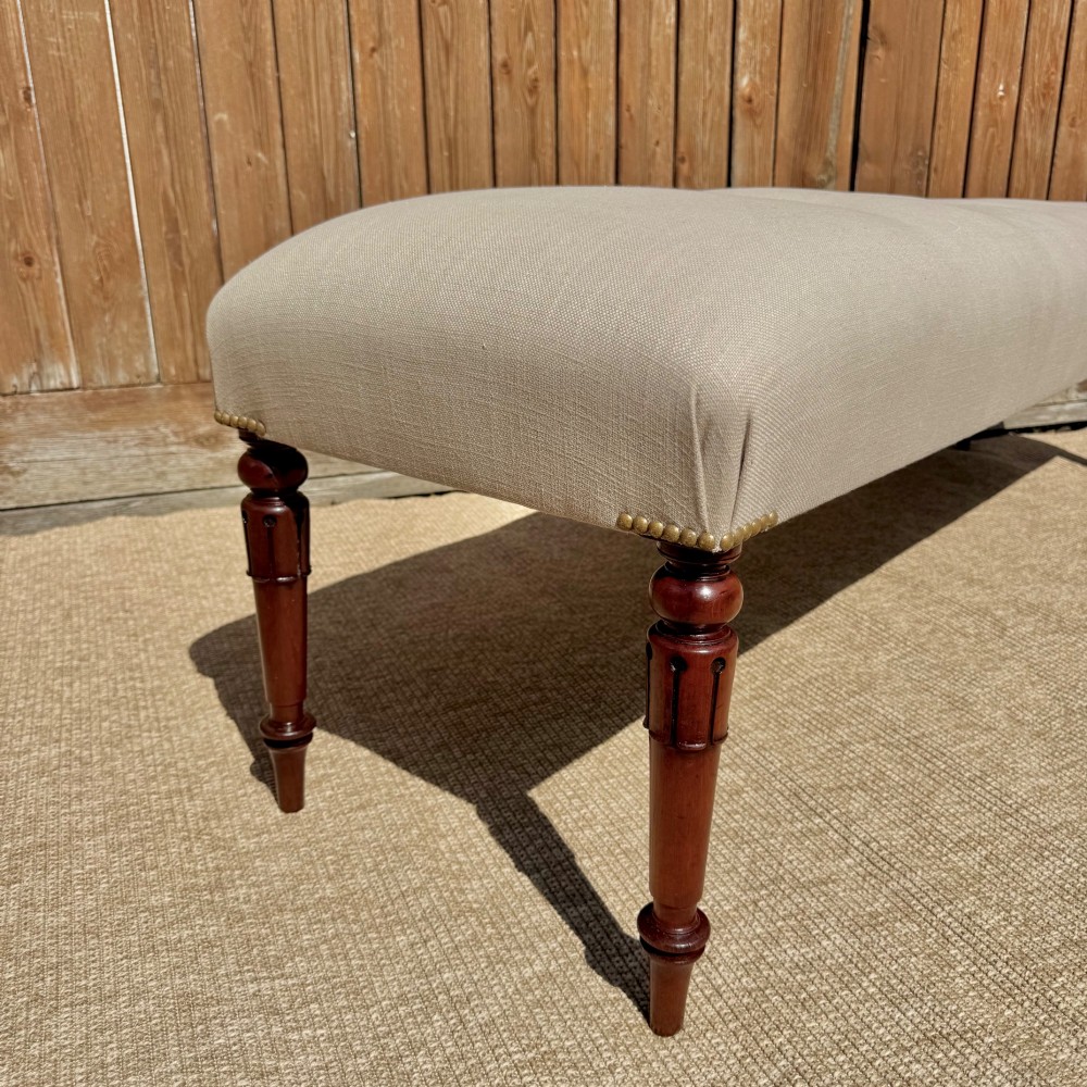 A long 185cm upholstered stool featuring a beige button-tufted linen top set on four turned dark wood legs. View IV