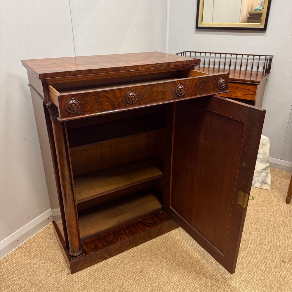 A Late Regency flame mahogany pier cabinet featuring carved rosette medallions on the upper frieze, flanking side columns with carved capitals, and a single solid wood door. View IV
