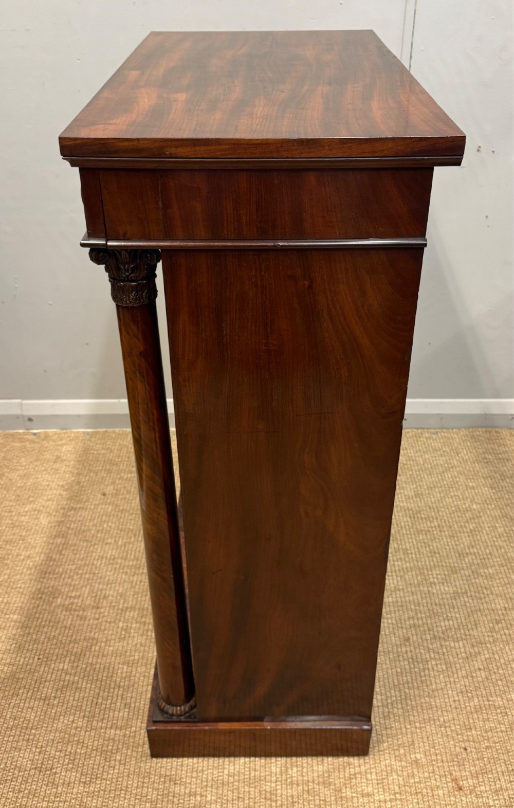 A Late Regency flame mahogany pier cabinet featuring carved rosette medallions on the upper frieze, flanking side columns with carved capitals, and a single solid wood door. View VIII