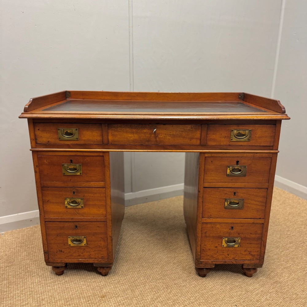 A Victorian military campaign kneehole desk in warm brown wood, featuring an inset leather writing surface, gallery rail, and seven drawers with flush brass handles.