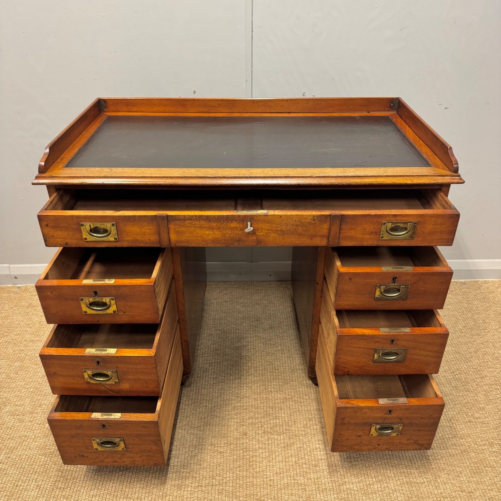 A Victorian military campaign kneehole desk in warm brown wood, featuring an inset leather writing surface, gallery rail, and seven drawers with flush brass handles. View IV