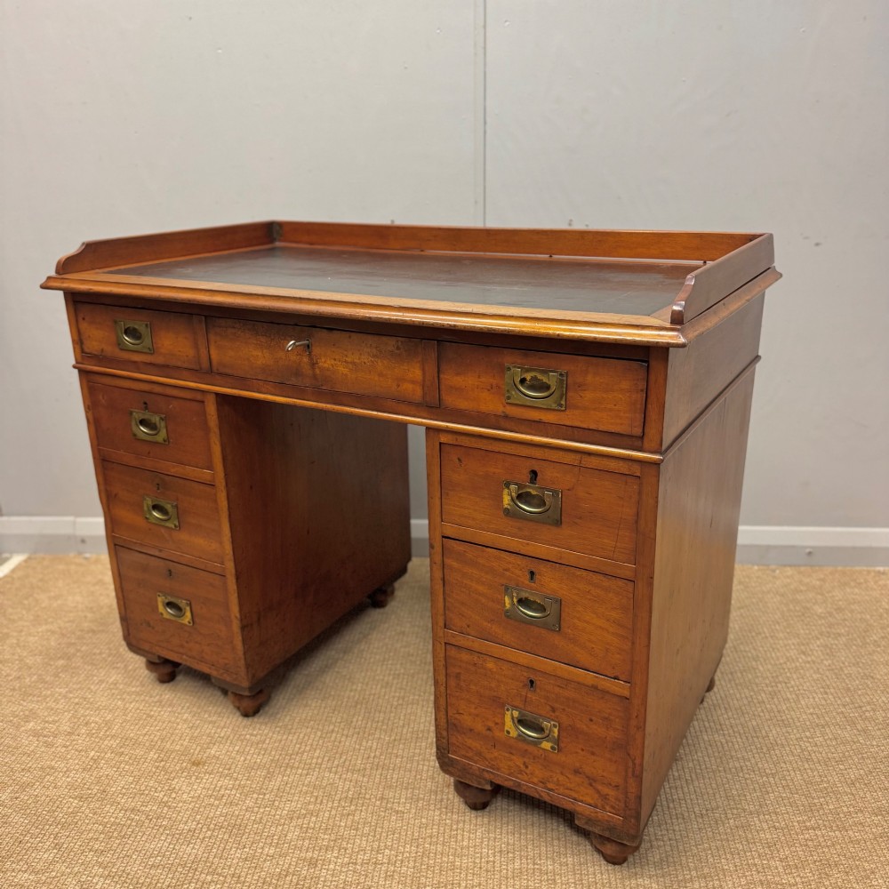 A Victorian military campaign kneehole desk in warm brown wood, featuring an inset leather writing surface, gallery rail, and seven drawers with flush brass handles. View V