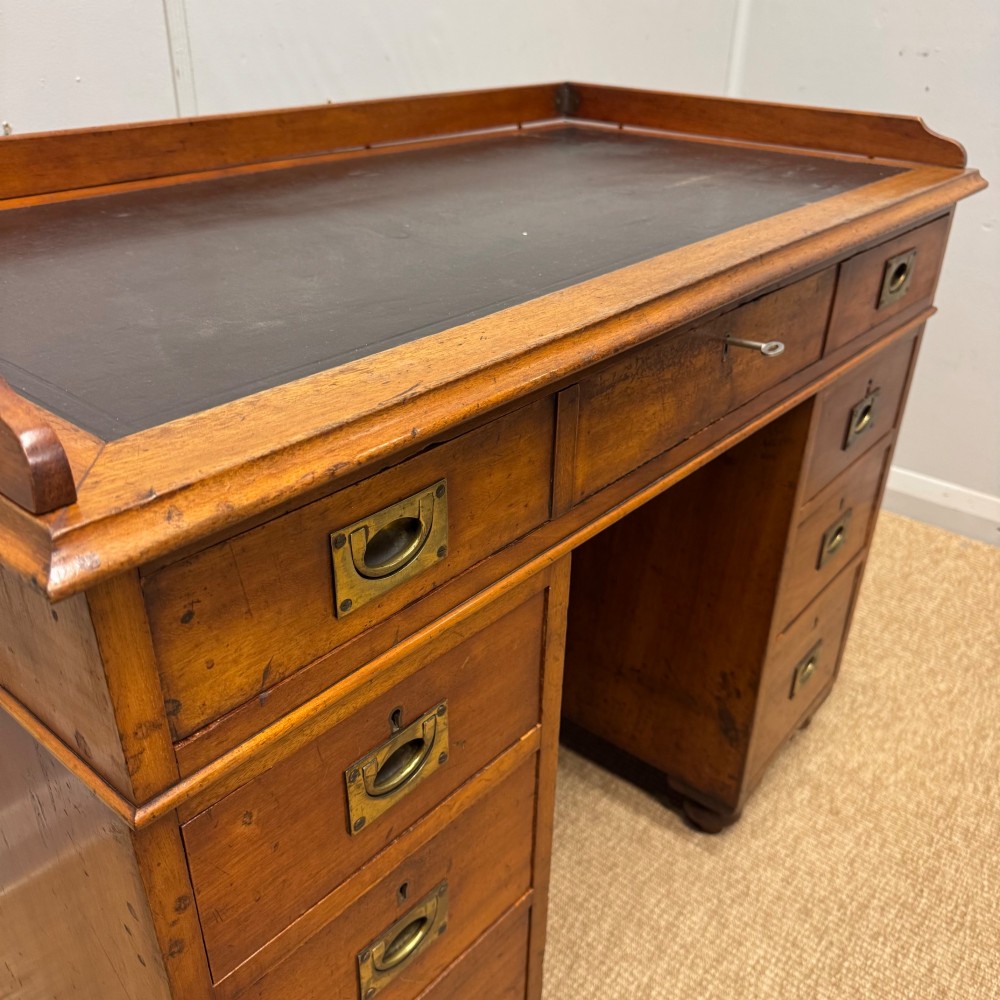 A Victorian military campaign kneehole desk in warm brown wood, featuring an inset leather writing surface, gallery rail, and seven drawers with flush brass handles. View VI
