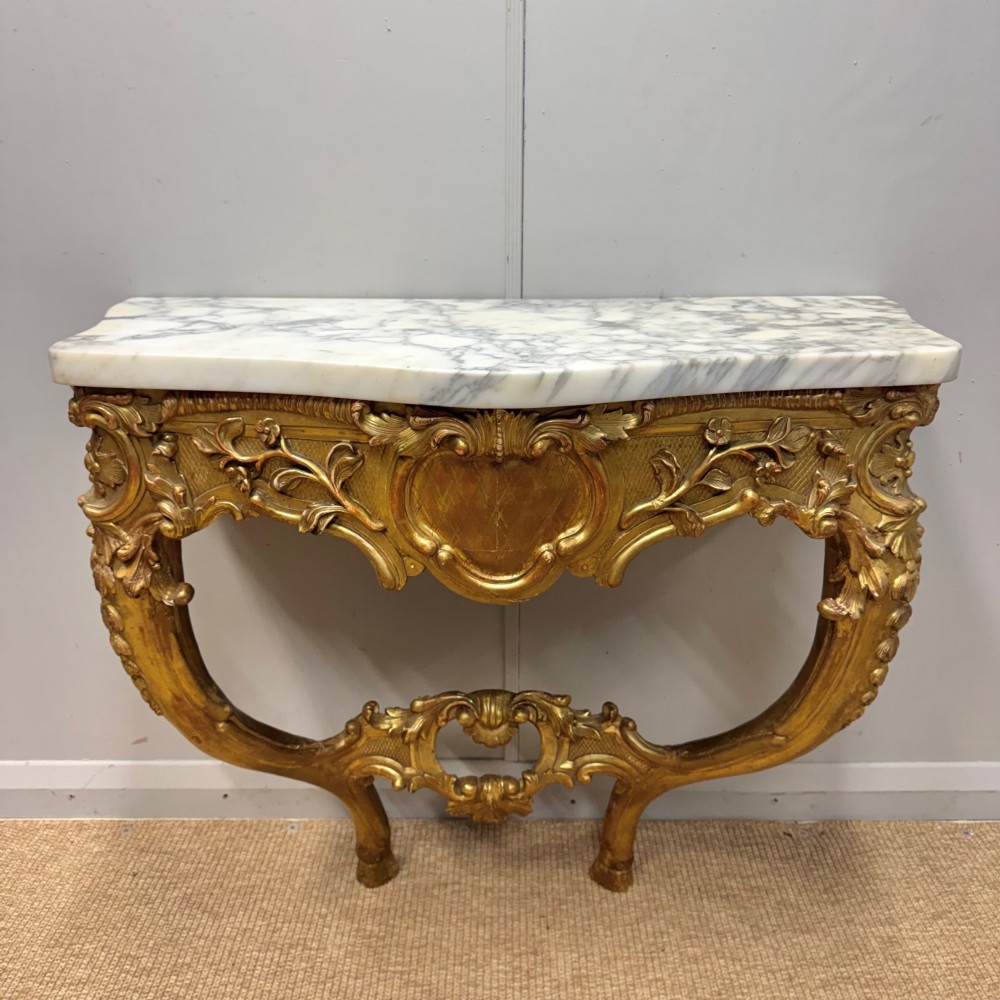 A French Louis XV style giltwood console table with heavily carved Rococo scrollwork, cabriole legs, and a white veined marble top.