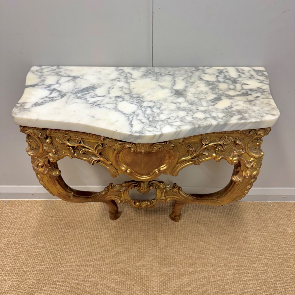 A French Louis XV style giltwood console table with heavily carved Rococo scrollwork, cabriole legs, and a white veined marble top. View III