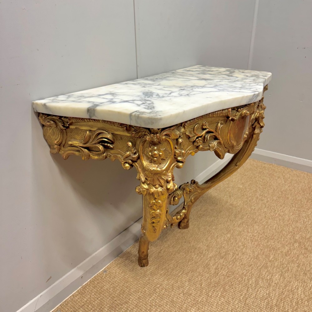 A French Louis XV style giltwood console table with heavily carved Rococo scrollwork, cabriole legs, and a white veined marble top. View IV