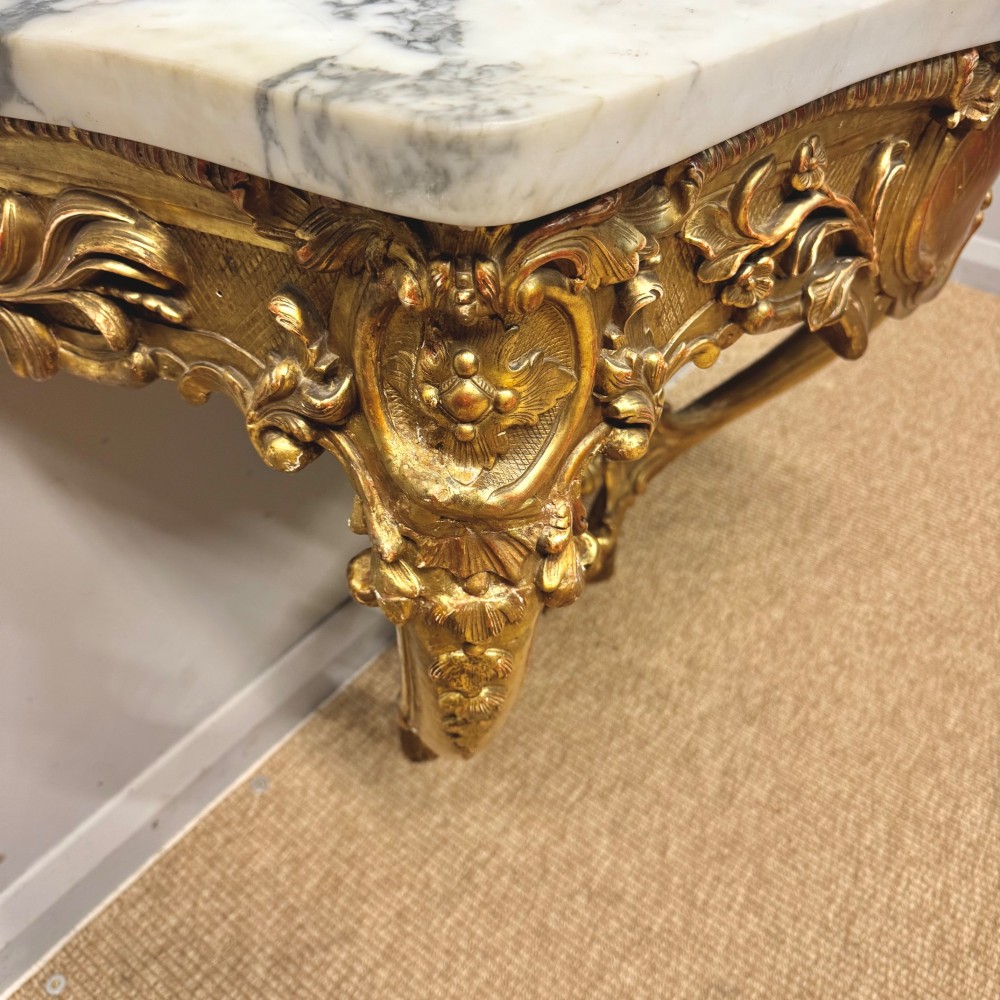 A French Louis XV style giltwood console table with heavily carved Rococo scrollwork, cabriole legs, and a white veined marble top. View V