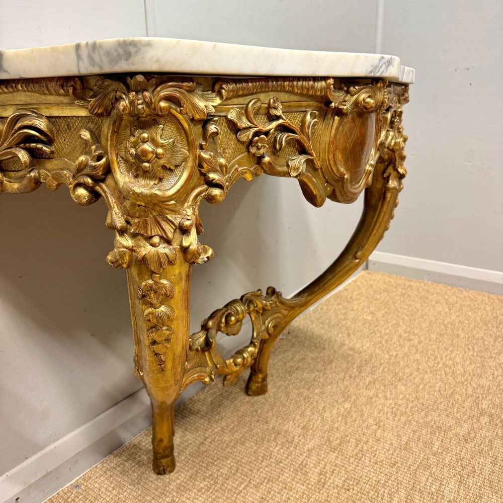A French Louis XV style giltwood console table with heavily carved Rococo scrollwork, cabriole legs, and a white veined marble top. View VI