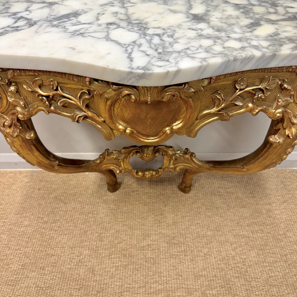 A French Louis XV style giltwood console table with heavily carved Rococo scrollwork, cabriole legs, and a white veined marble top. View VIII