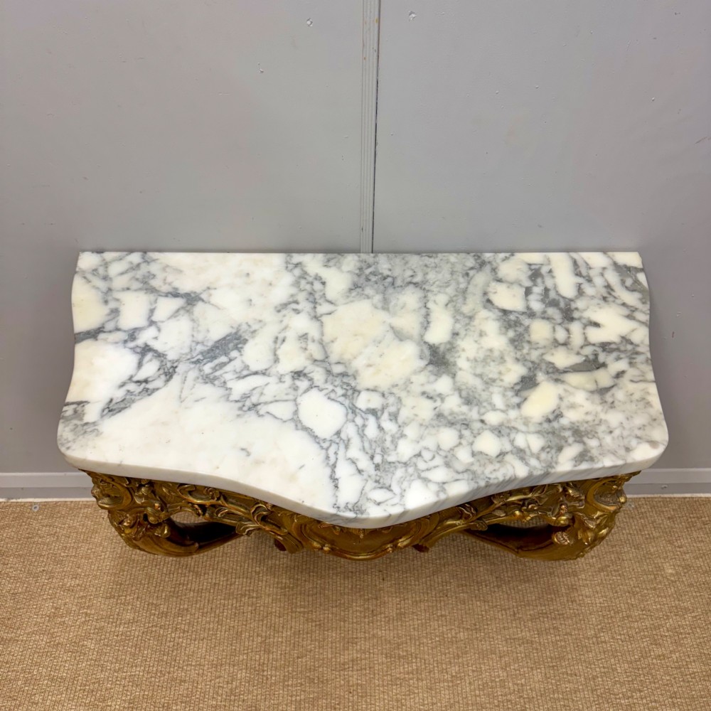 A French Louis XV style giltwood console table with heavily carved Rococo scrollwork, cabriole legs, and a white veined marble top. View IX