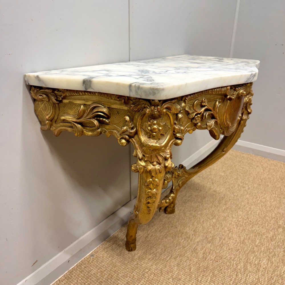 A French Louis XV style giltwood console table with heavily carved Rococo scrollwork, cabriole legs, and a white veined marble top. View X