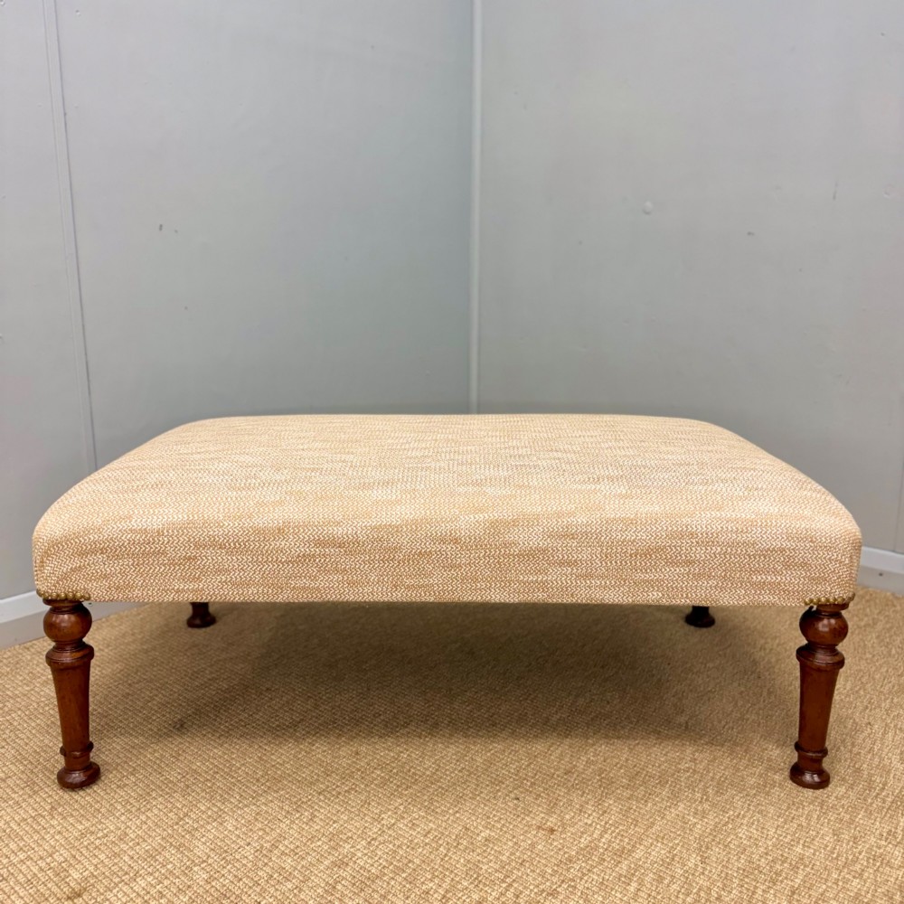 A rectangular upholstered footstool covered in beige chenille fabric, featuring brass stud trim at the corners and four turned wooden legs. View II