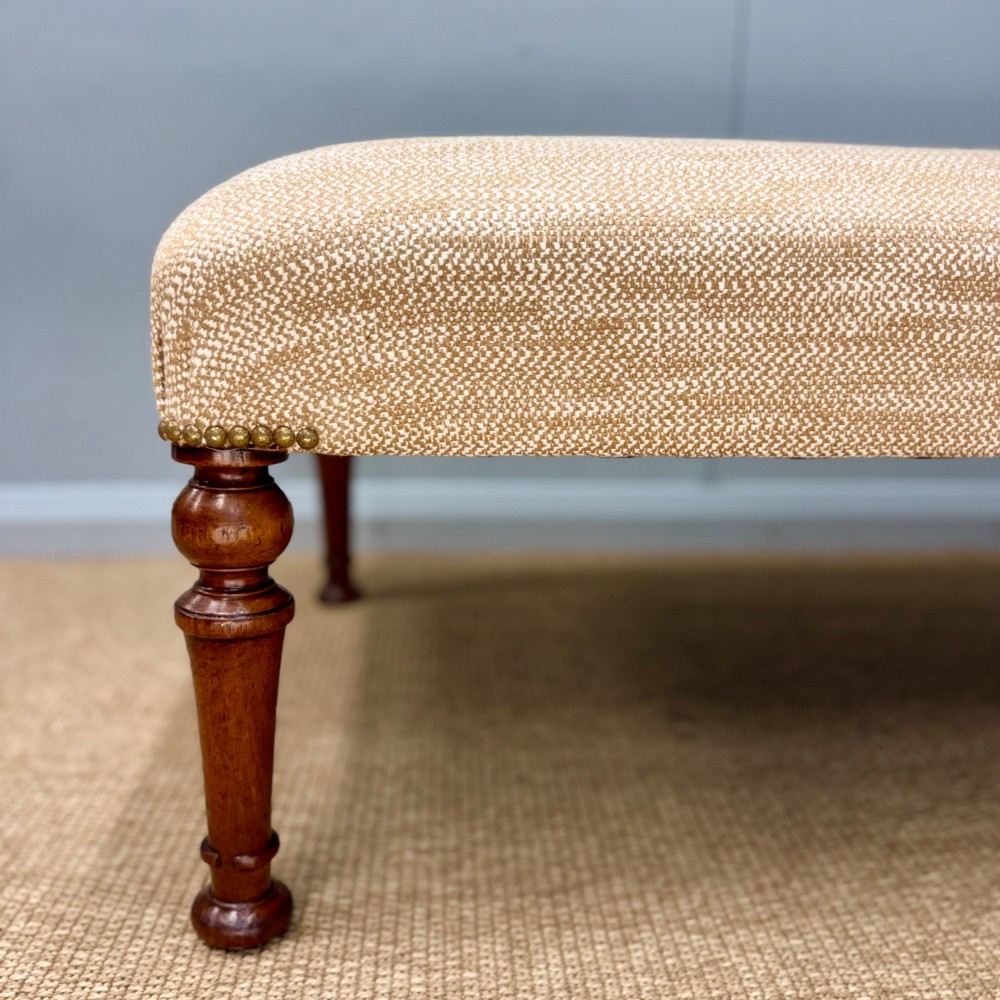 A rectangular upholstered footstool covered in beige chenille fabric, featuring brass stud trim at the corners and four turned wooden legs. View III