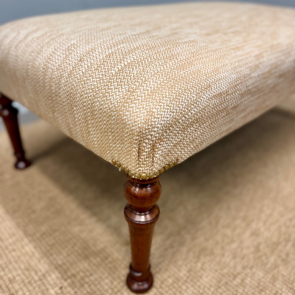 A rectangular upholstered footstool covered in beige chenille fabric, featuring brass stud trim at the corners and four turned wooden legs. View IV