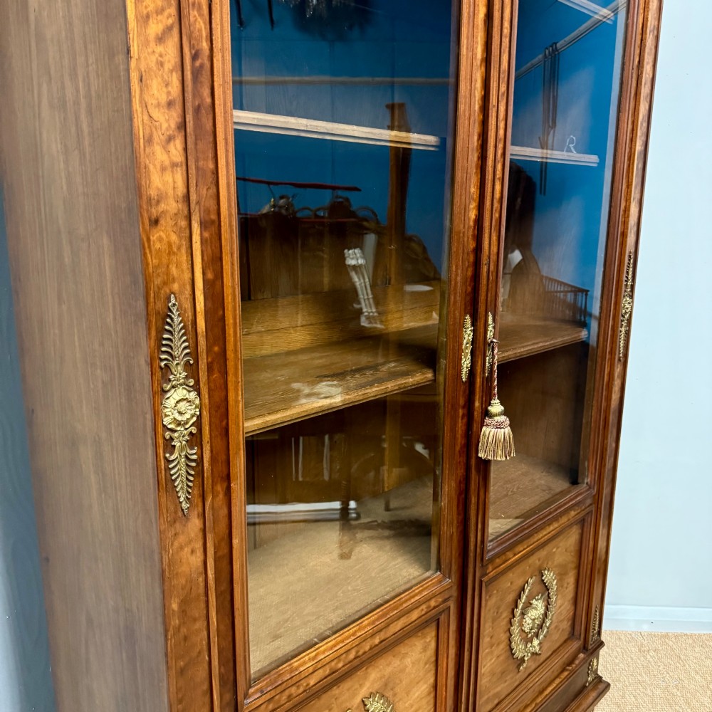 A tall French Empire style warm brown timber bookcase featuring two glass-fronted doors, gilt brass laurel wreath mounts, and adjustable interior shelves. View V