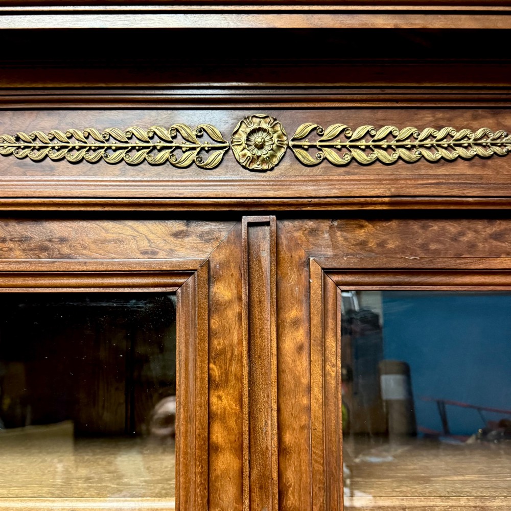 A tall French Empire style warm brown timber bookcase featuring two glass-fronted doors, gilt brass laurel wreath mounts, and adjustable interior shelves. View VII
