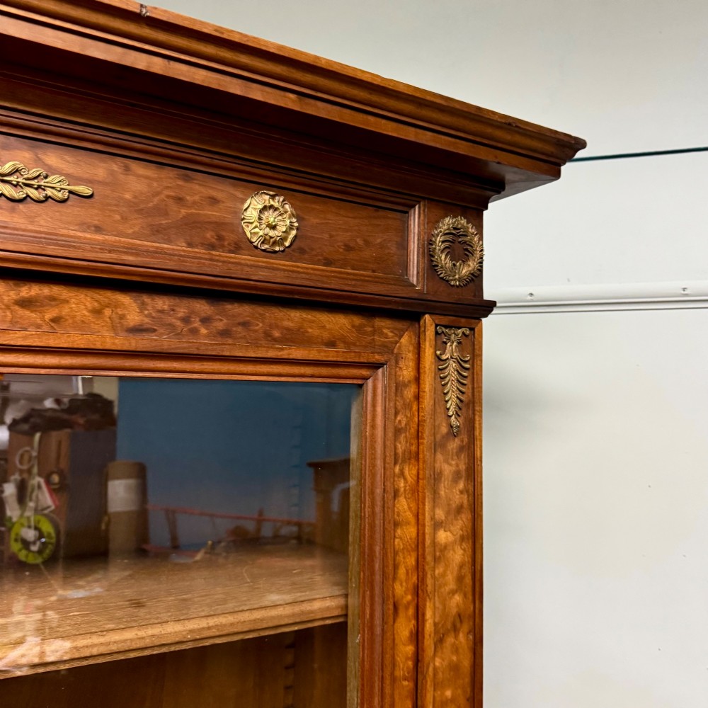 A tall French Empire style warm brown timber bookcase featuring two glass-fronted doors, gilt brass laurel wreath mounts, and adjustable interior shelves. View VIII