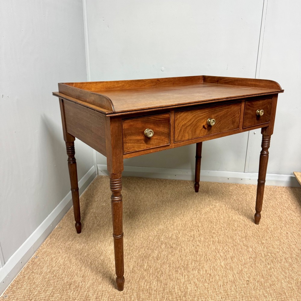 A Regency mahogany dressing table featuring three drawers with round brass knobs, a raised gallery top, and four turned tapered legs.