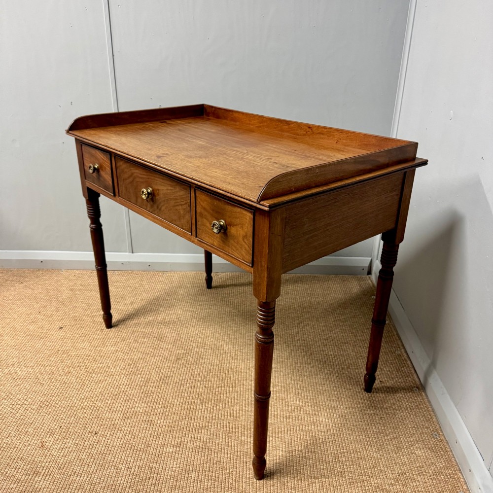 A Regency mahogany dressing table featuring three drawers with round brass knobs, a raised gallery top, and four turned tapered legs. View V