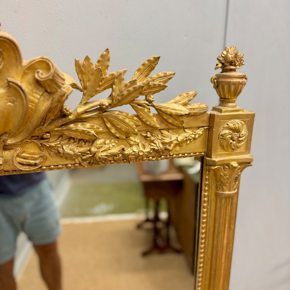 A large rectangular French Louis XVI style water gilded mirror featuring fluted side pilasters and an elaborate carved crest with laurel leaves and urn finials. View IV
