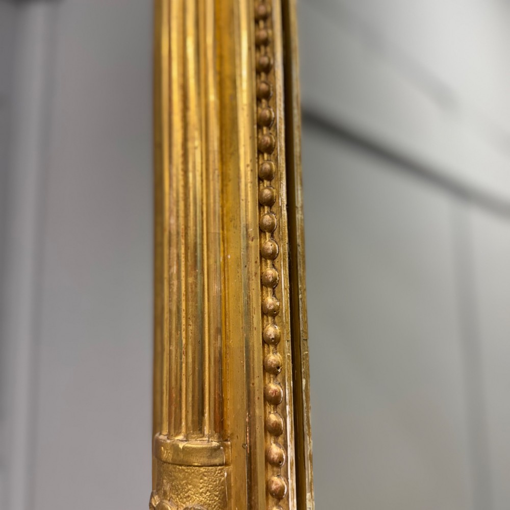A large rectangular French Louis XVI style water gilded mirror featuring fluted side pilasters and an elaborate carved crest with laurel leaves and urn finials. View V