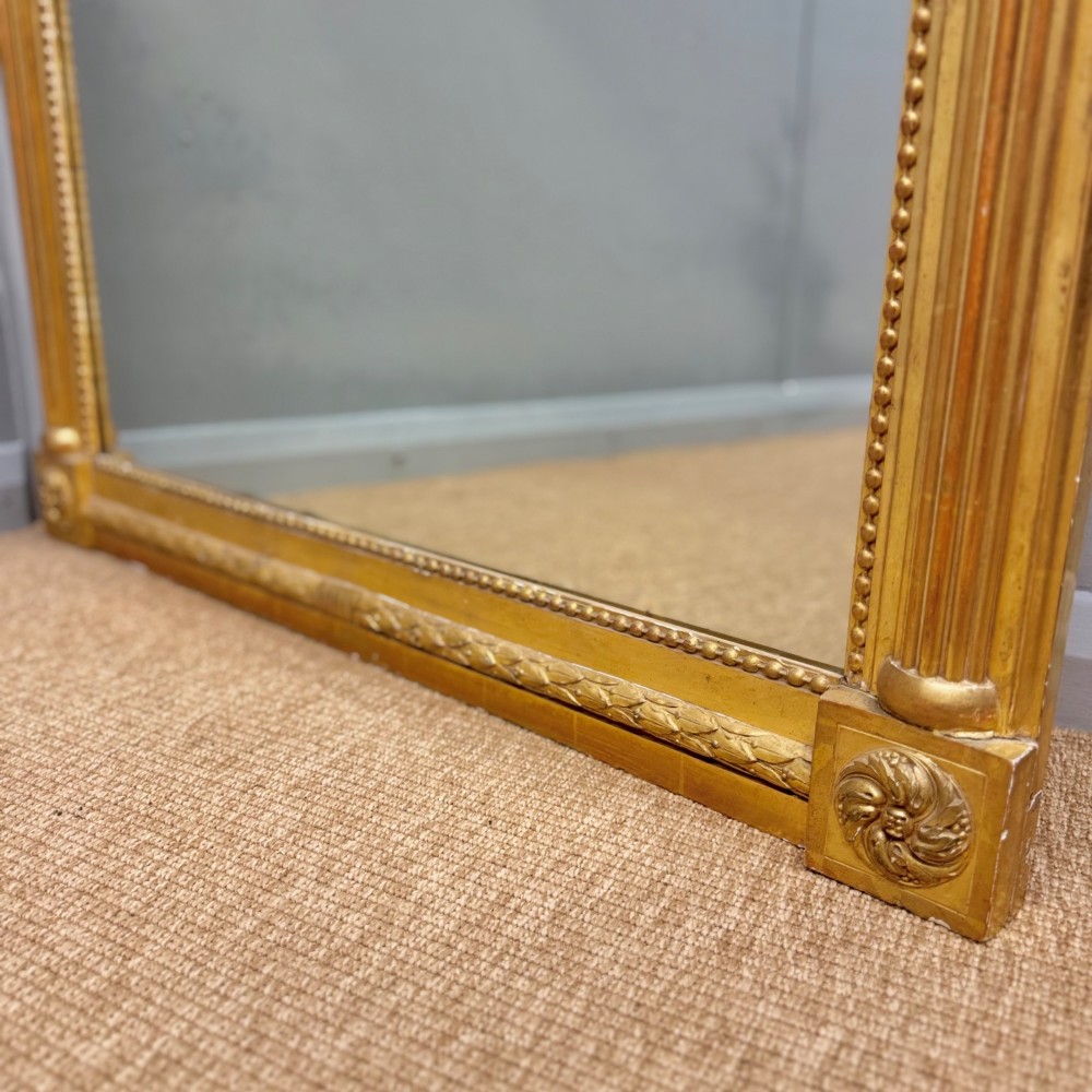 A large rectangular French Louis XVI style water gilded mirror featuring fluted side pilasters and an elaborate carved crest with laurel leaves and urn finials. View VI