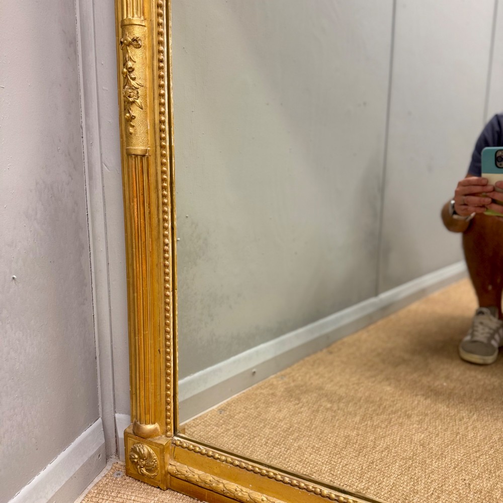 A large rectangular French Louis XVI style water gilded mirror featuring fluted side pilasters and an elaborate carved crest with laurel leaves and urn finials. View VII