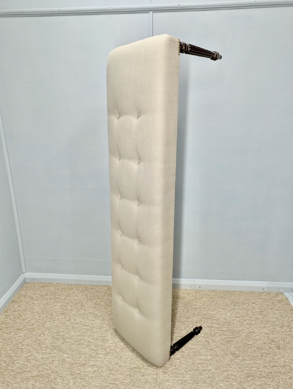 A long upholstered bench in neutral fabric featuring brass stud trim and dark fluted wooden legs. View III