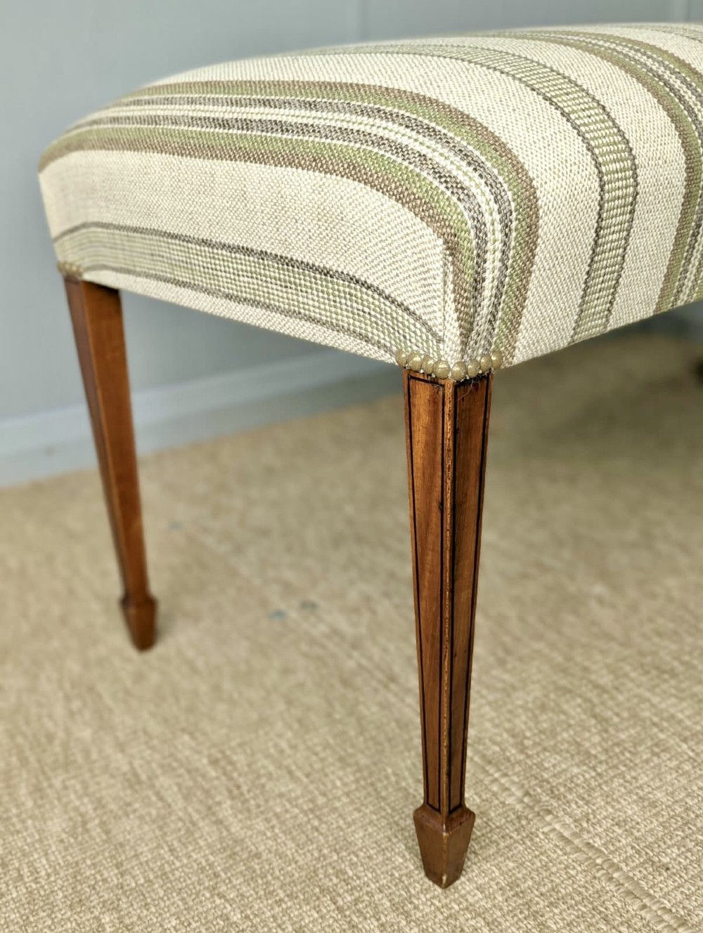 An Edwardian rectangular satinwood piano stool upholstered in beige striped fabric with square tapered legs. View II