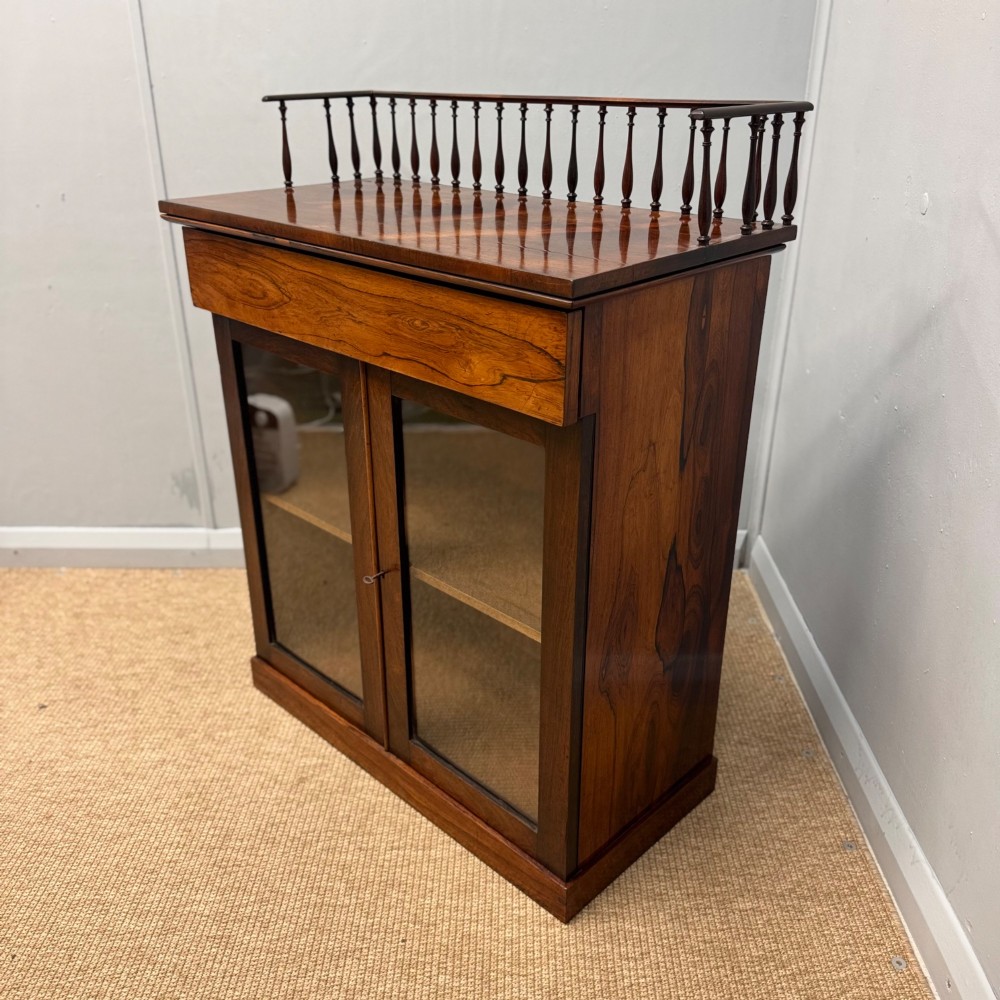 A dark brown Regency rosewood pier cabinet featuring a spindle gallery top, plain apron, and twin glazed doors resting on a plinth base. View V