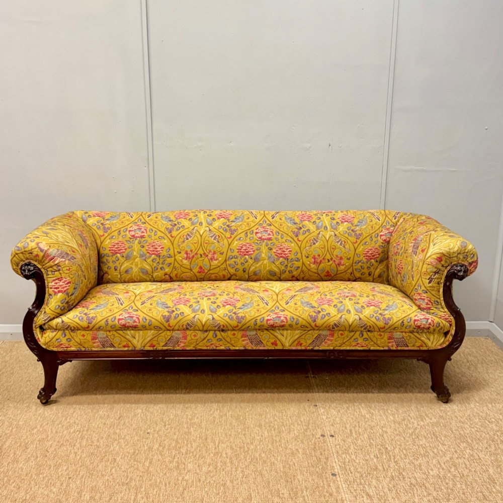 A Late Regency mahogany sofa featuring scroll arms, carved lion mask details, and yellow botanical William Morris style upholstery.