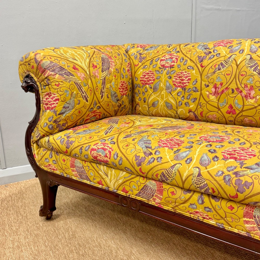 A Late Regency mahogany sofa featuring scroll arms, carved lion mask details, and yellow botanical William Morris style upholstery. View V