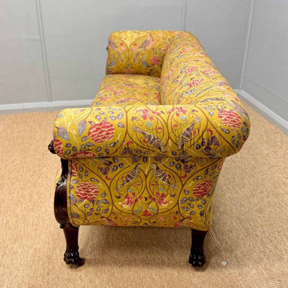 A Late Regency mahogany sofa featuring scroll arms, carved lion mask details, and yellow botanical William Morris style upholstery. View VII