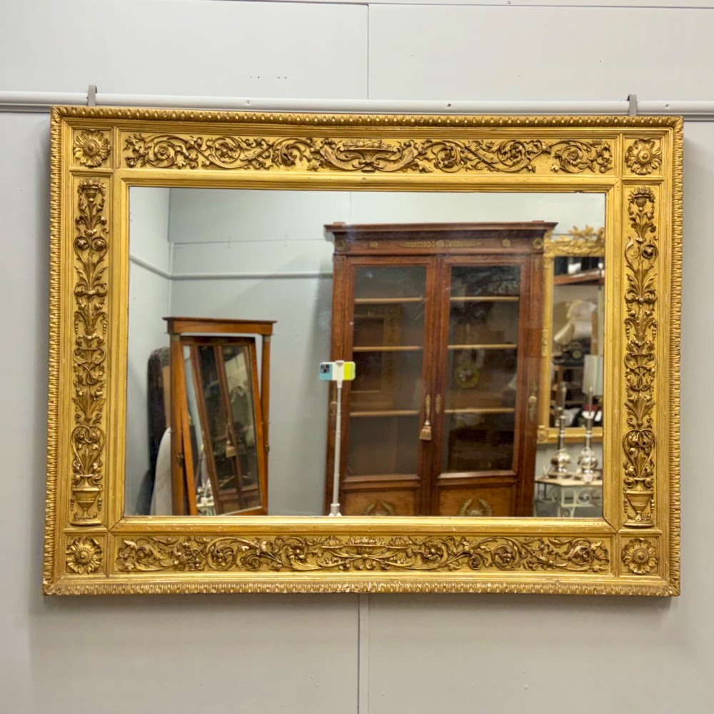 A large horizontal rectangular mirror featuring an intricately carved giltwood frame with classical urn, floral, and leaf motifs.