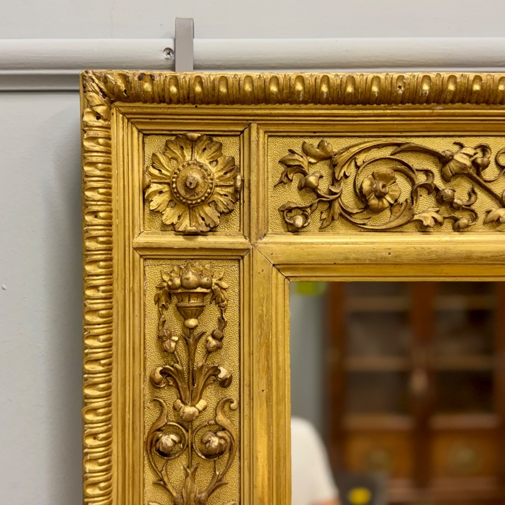A large horizontal rectangular mirror featuring an intricately carved giltwood frame with classical urn, floral, and leaf motifs. View III