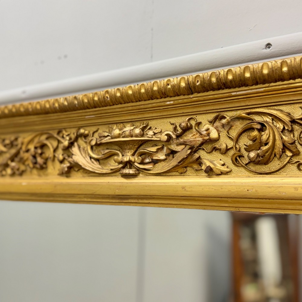 A large horizontal rectangular mirror featuring an intricately carved giltwood frame with classical urn, floral, and leaf motifs. View V