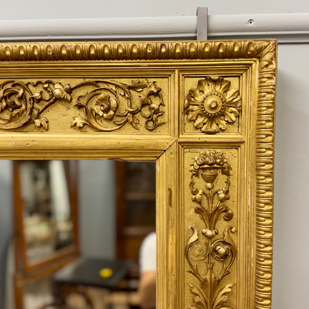 A large horizontal rectangular mirror featuring an intricately carved giltwood frame with classical urn, floral, and leaf motifs. View VI