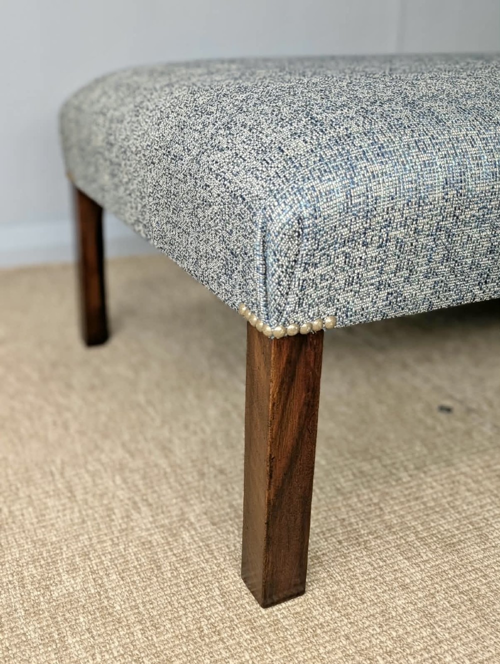 A large rectangular upholstered footstool covered in blue woven fabric with dark square wooden legs and brass stud detailing. View II