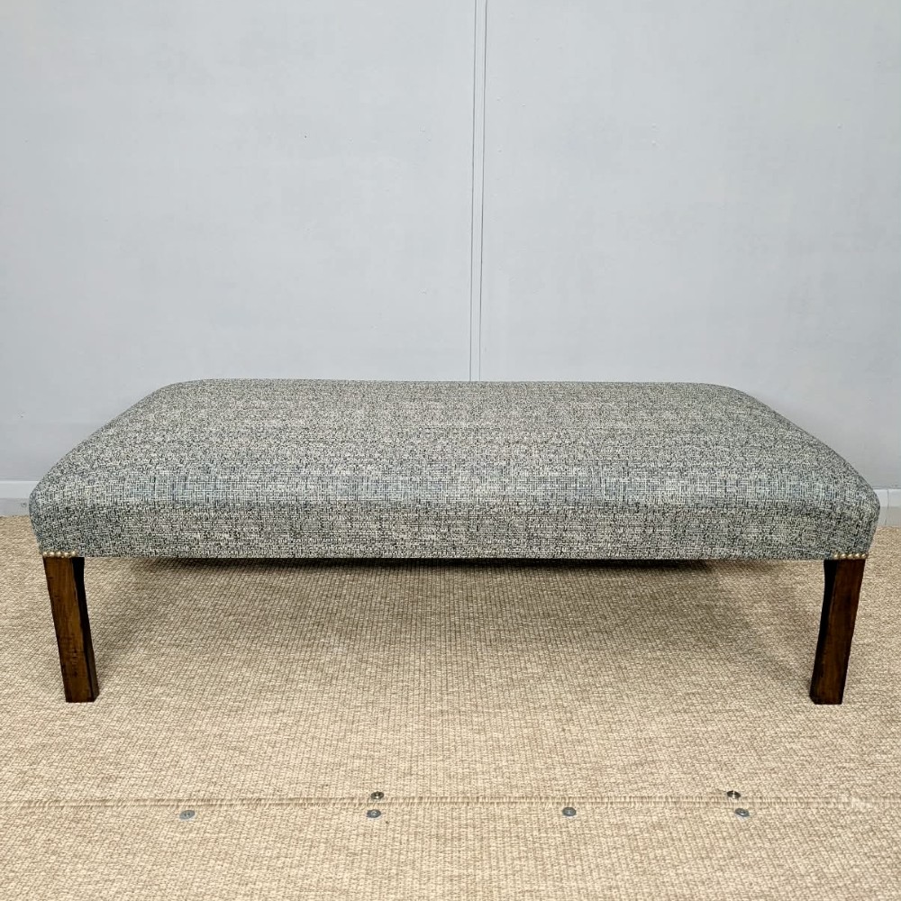 A large rectangular upholstered footstool covered in blue woven fabric with dark square wooden legs and brass stud detailing. View III