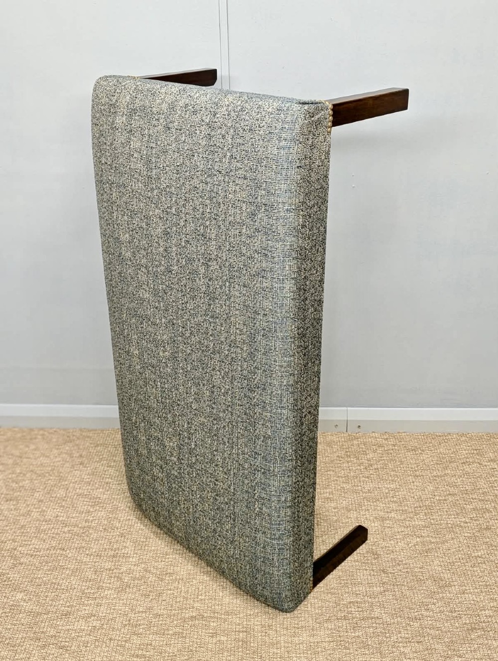 A large rectangular upholstered footstool covered in blue woven fabric with dark square wooden legs and brass stud detailing. View V