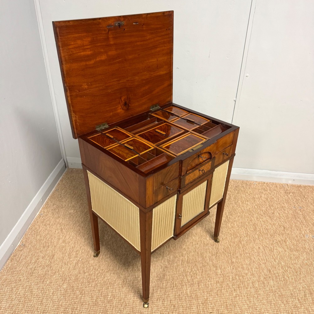 A late Georgian mahogany work table with an open hinged lid revealing fitted interior compartments, pleated fabric side panels, and square tapered legs on brass castors.